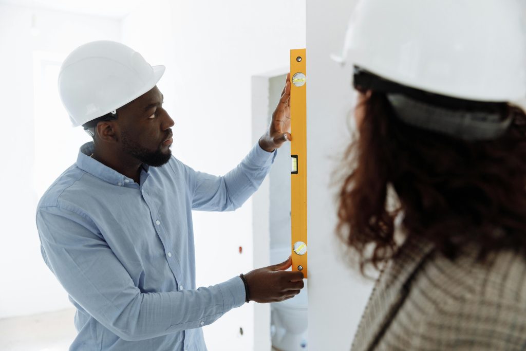An adult man in safety gear uses a spirit level indoors for accurate measurements.