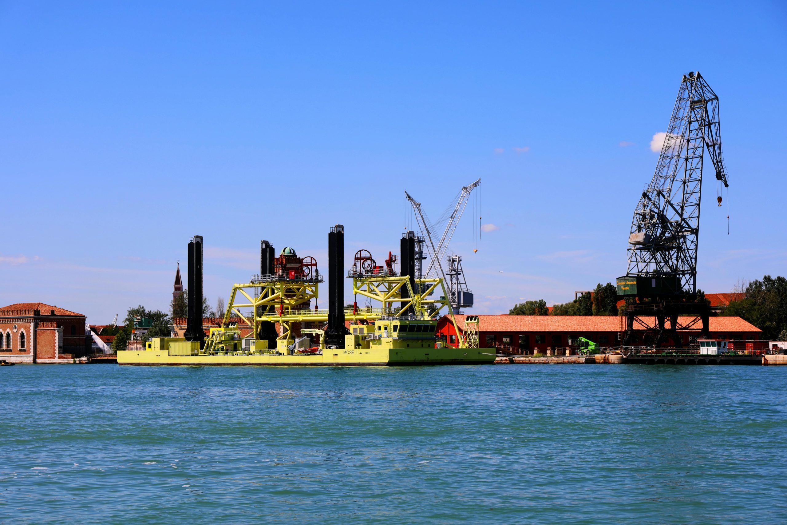 View of industrial watercraft and cranes against the historic backdrop of Venice, Italy.